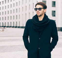 Fashion and Style. A young man in a fashionable black coat and sunglasses posing near the business center. Outdoor.