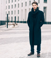 Fashion portrait handsome elegant man wearing black coat in winter day over snowy bussines street background