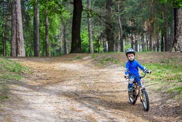 Fototapeta premium Happy cute blond kid boy having fun his first bike on sunny summer day, outdoors. child making sports. Active leisure for children. wear safety helmet. is smiling and cicling