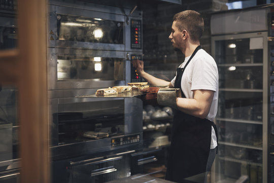 Man baker preparing food for baking in oven.