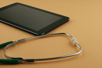 Stethoscope and tablet computer on orange background.