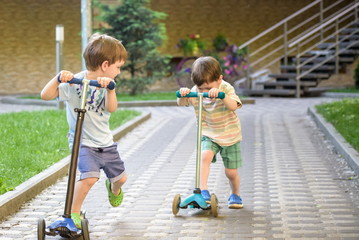 Two cute boys, compete in riding scooters, outdoor in the park,
