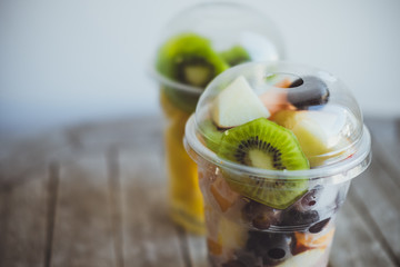 Fresh Fruits in Plastic Cups for takeaway: kiwi, pineapple, tangerines, apples, melon in plastic cups on the wooden table