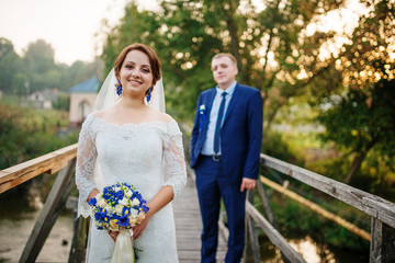 Cheerful wedding couple on wooden bridge at sunset.