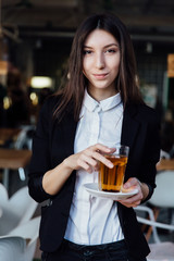 young cute brunette girl business in the interior hipster cafes holding a glass of tea.