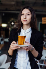 young cute brunette girl business in the interior hipster cafes holding a glass of tea.