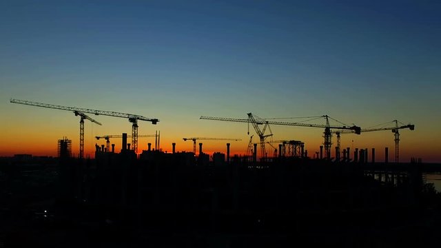 silhouette of cranes working on construction site on sunset sky background.
