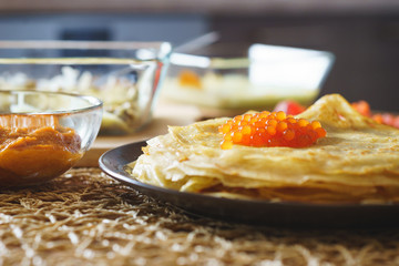 Tasty snack on a wooden table - pancakes with red caviar and eggplant caviar.