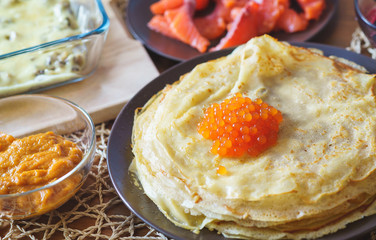 Closeup tasty snack on a wooden table - pancakes with red caviar and smoked fish