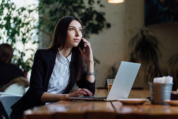 Beautiful young business woman student with a phone and a laptop in a cafe. Long hair brunette.