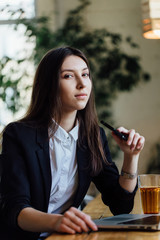 Beautiful young business woman student with a phone and a laptop in a cafe. Long hair brunette.