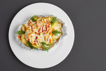 Top view of fried in foil sea fish and potato with paprica and cheese on gray background