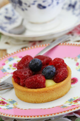 Delicious tartelette with custard, fresh raspberries and blueberries on pink plate
