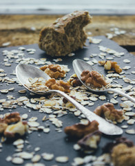 Two vintage spoons different shapes on the slate Board, scattered with oatmeal, walnuts and bread crumbs