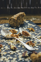 Two vintage spoons different shapes on the slate Board, scattered with oatmeal, walnuts and bread crumbs