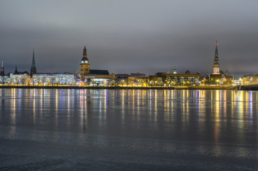 Fototapeta na wymiar View of the old city of Riga with its bright lights in Latvia over the frozen river Daugava at night in winter