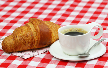Fresh croissant with cup of black coffee on checkered cloth
