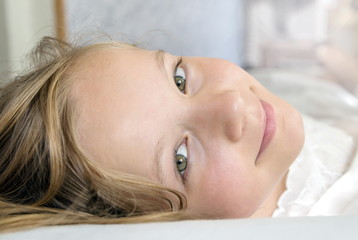 A little blonde girl with beautiful eyes is lying in bed