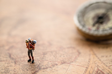 Miniature people : travellers standing on world map in front of vintage compass,  exploring on earth background concept.