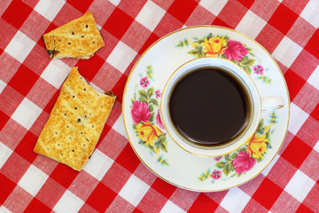 Cup of black tea in vintage cup and biscuit on checkered red and white cloth shot from above
