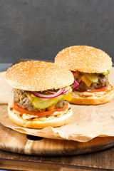 Fresh burger with beef on wooden table and paper. Gray background.