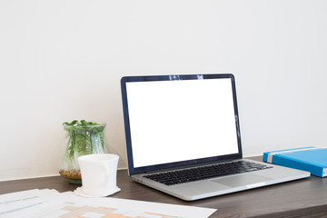 Fototapeta premium office table with blank screen on laptop, cup of coffee, business report paper and garden tree on glass vase.
