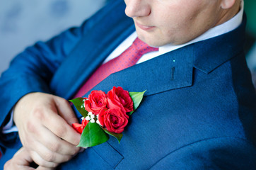 man in a dark blue suit corrects hand of a red rose boutonniere