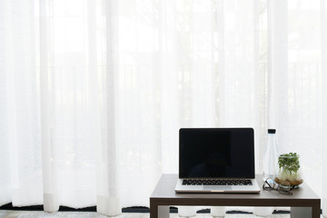 office table with blank screen laptop , bottle of water , garden tree vase on white drape background.