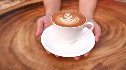 Hands holding a cup of hot latte cappuccino coffee on wood table