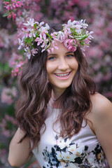 smiling young woman with a wreath on her head on a background of flowering spring trees