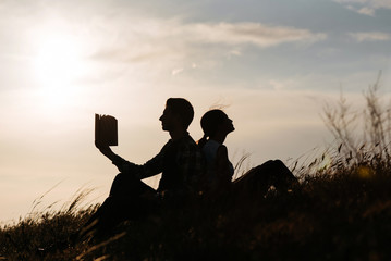 Fototapeta na wymiar Silhouette of man and girl read book at sunset