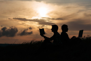 Fototapeta na wymiar silhouette of two man at sunset who work at notebook and read book
