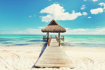 Tropical white sandy beach. Palm leaf roofed wooden pier with gazebo on the beach. Cross processed....