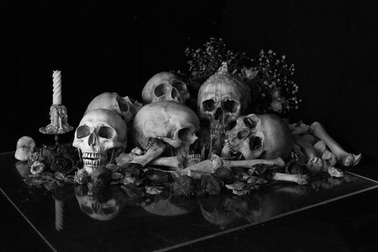 Pile of skulls with bone and pile of withered dry flowers with candle light on plastic plate