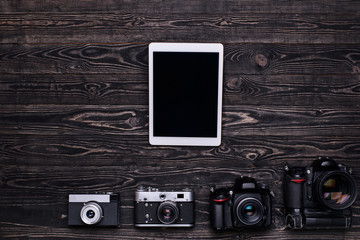 Top view photo of cameras and tablet computer/Retro cameras,modern DSLR cameras and tablet computer on dark wooden table