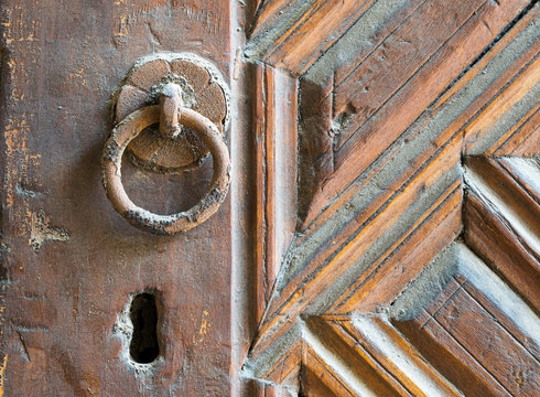 Closeup of rusted ring door knob over an aged decorated wooden door