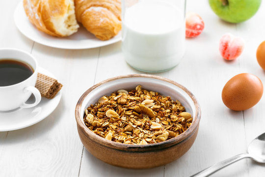 Oatmeal muesli with nuts, croissants, fruits, milk and coffee for delicious breakfast. Traditional healthy meal for breakfast on a table.