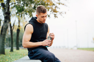 Athlete resting on bench in park after running with bottle of water. Rest  a hard workout.