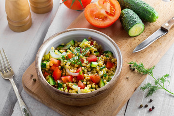 Salad made of couscous with vegetables in a bowl for healthy meal. Cooking of traditional Israeli Ptitim for lunch. Moroccan food and ingredients on a table. Top view.