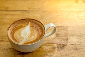 Cup of frothy cappucino on a wooden table with lots of room for copyspace.  This yummy and delicious creamy drink is part of your morning routine and helps you wake up.  Organic beans.