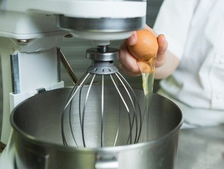 A fresh free range egg being cracked into an industrial metal whisking machine. Shot with a shallow depth of field.