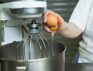 A fresh free range egg being cracked into an industrial metal whisking machine. Shot with a shallow depth of field.