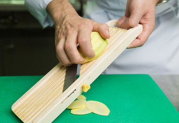 A fresh young green organic mango, being hand sliced into thins slices on a green cutting board