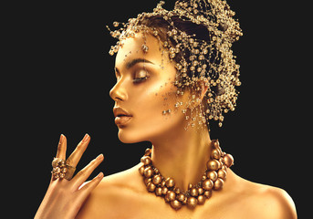 Gold woman skin. Beauty fashion model girl with golden makeup, hair and jewellery on black...