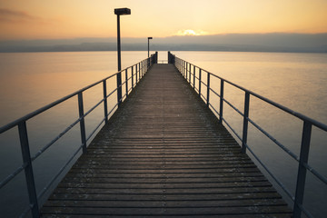 Fototapeta na wymiar Ein symmetrischer ruhiger Holzsteg am Bodensee bei Sonnenuntergang 