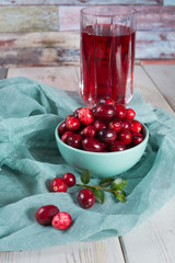 Red cranberry juice in a glass, cranberries in the green clay bowl on the table
