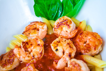 Fresh pasta with shrimp and tomato sauce with basil in a white bowl.
