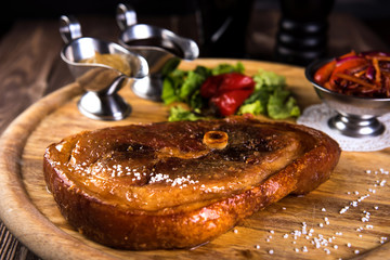 Roasted slice of pork leg with bone. Two sauces, Red beans, onion, bell pepper on wooden background and black glass of beer.