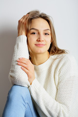 Young beautiful woman sitting in a white sweater with her hands near the head