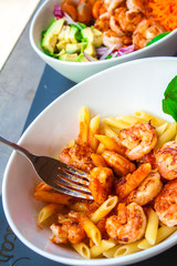 Fresh pasta with shrimp and tomato sauce with basil in a white bowl.
